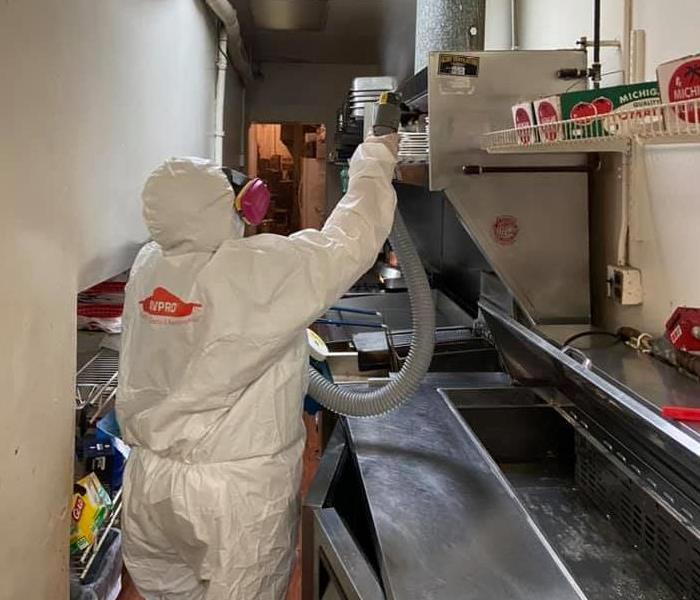 Technician in full PPE sanitizing commercial kitchen